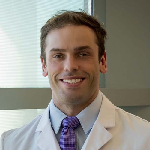 Dr. Boyd, a smiling man with brown hair, wearing a lab coat over a white shirt and purple tie.