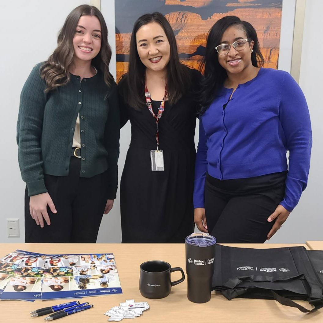 Three women pose together in front of table