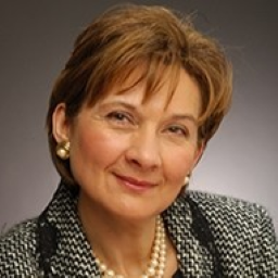 headshot of white woman with red hair wearing a black and white checked jacket