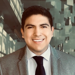 smiling man with dark wavy hair in gray suit with white shirt and black tie