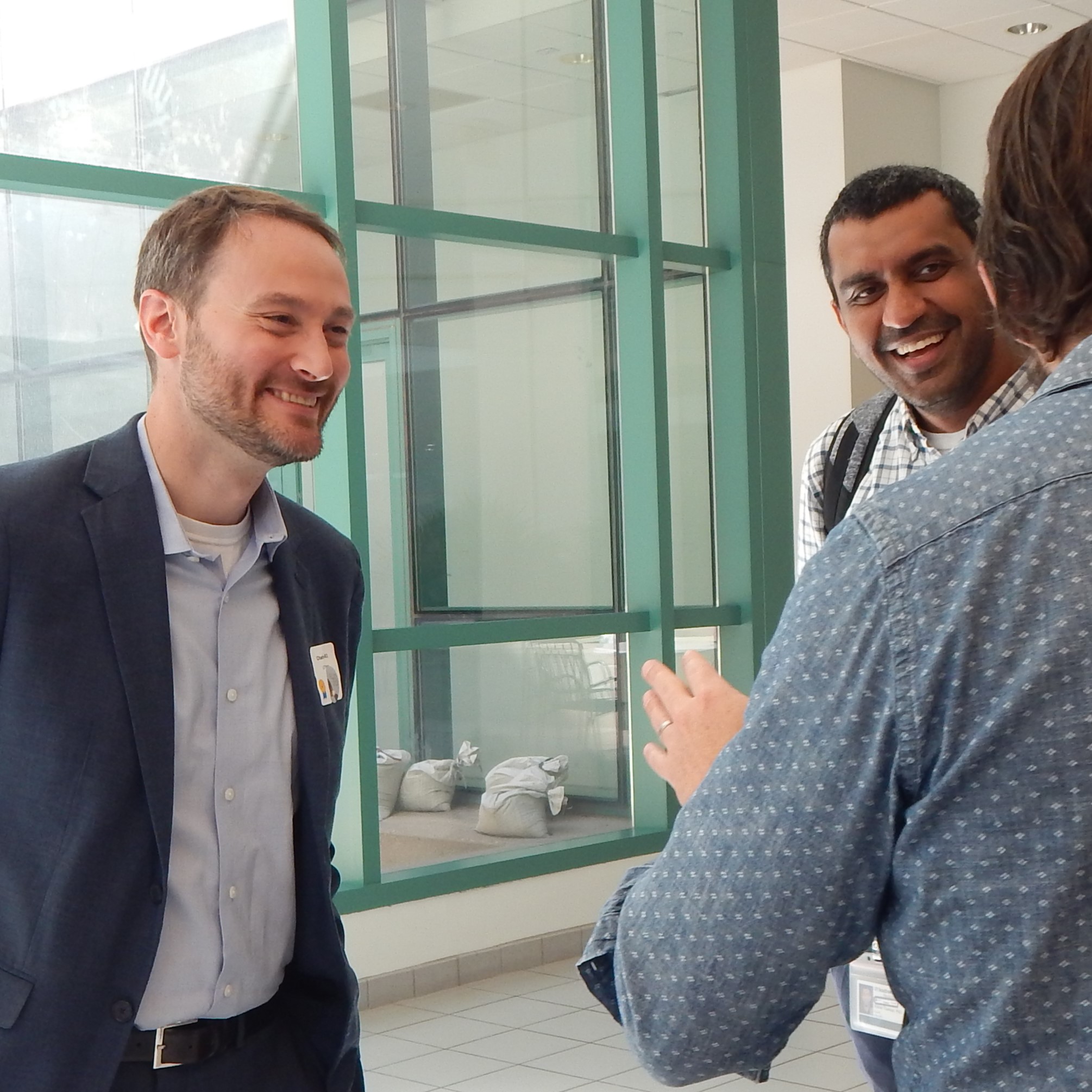 three men talking in atrium area in front of windows