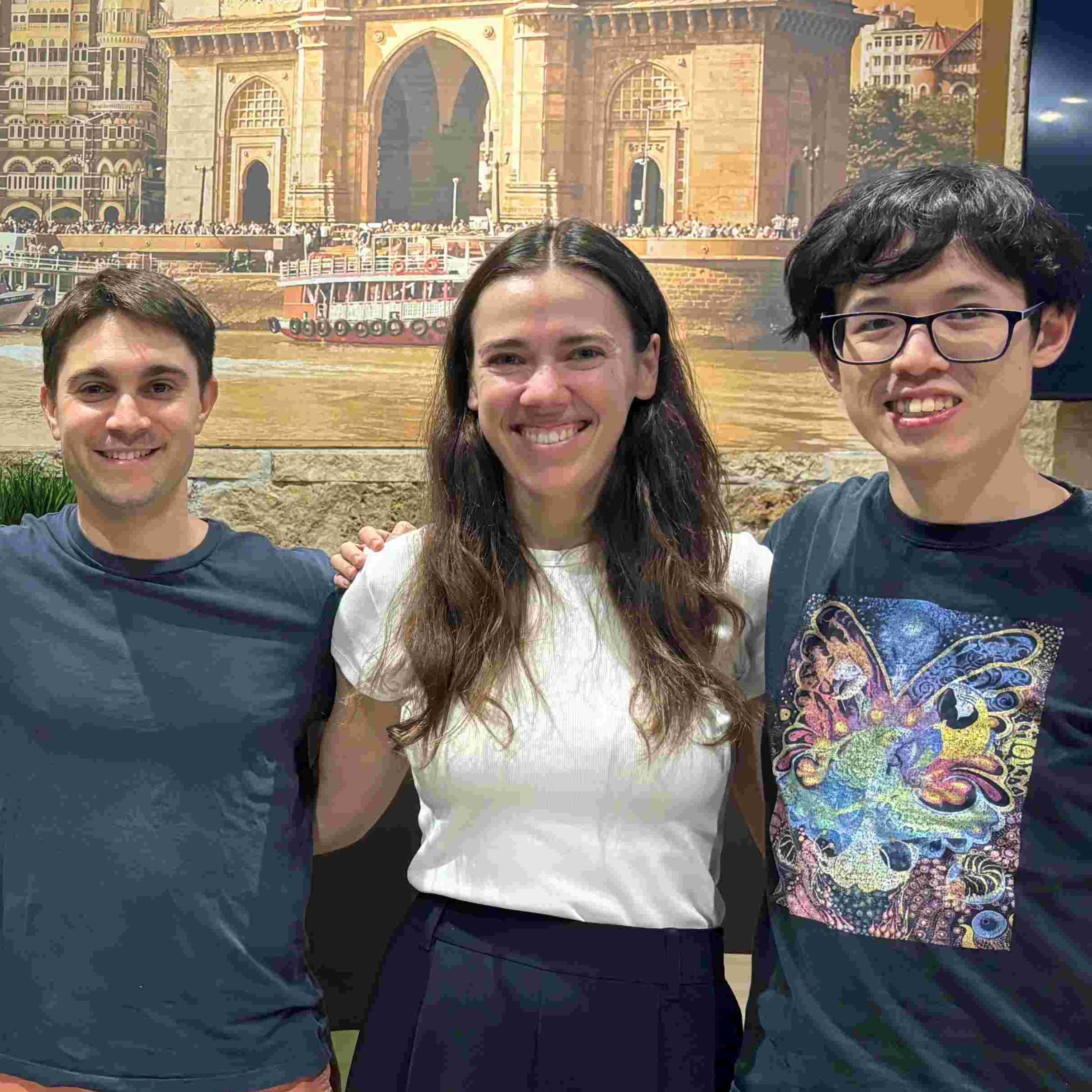 3 smiling people with arms around each other, from left: dark haired young white man in tshirt, white woman with long dark hair in white shirt, person with short dark hair in print tshirt and glasses