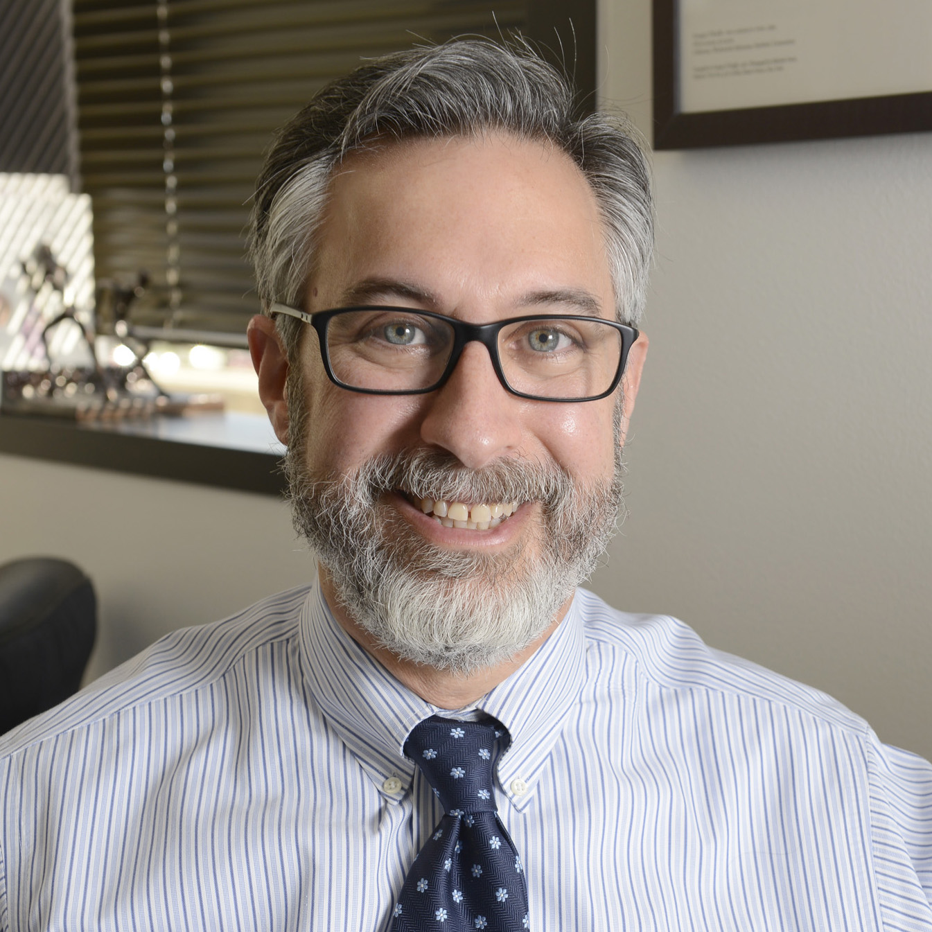 Adam Brenner, M.D. headshot; smiling white man with glasses, greying hair and beard wearing striped blue shirt and polkadot blue tie