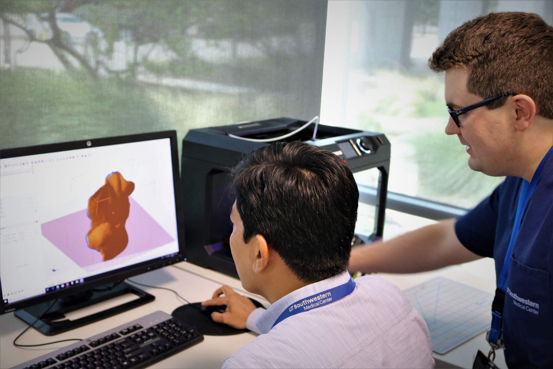 A man sitting down and a man standing up look at a computer monitor.