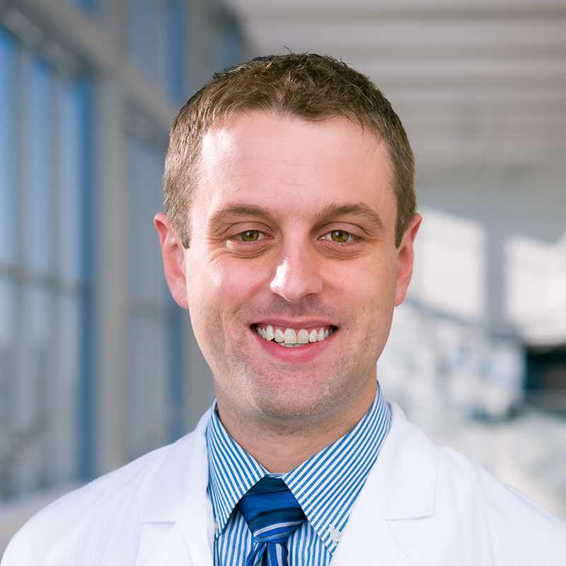 Smiling man with short brown hair, wearing a white lab coat.
