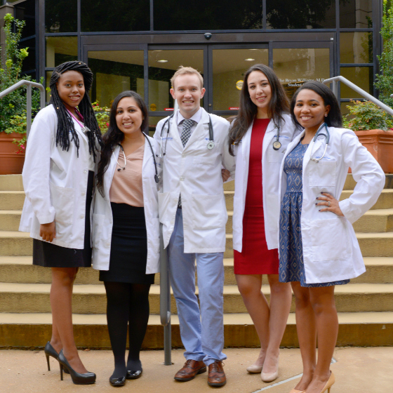 Four female medical students and a male medical student stand in front of a building on the UT Southwestern campus