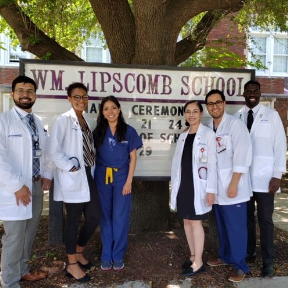 Three female and three male medical students stand in front of an elementary school sign