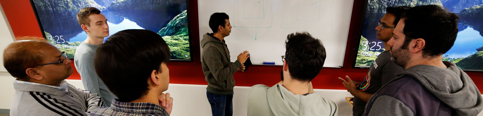 Male students gather around as a classmate develops an idea on a whiteboard