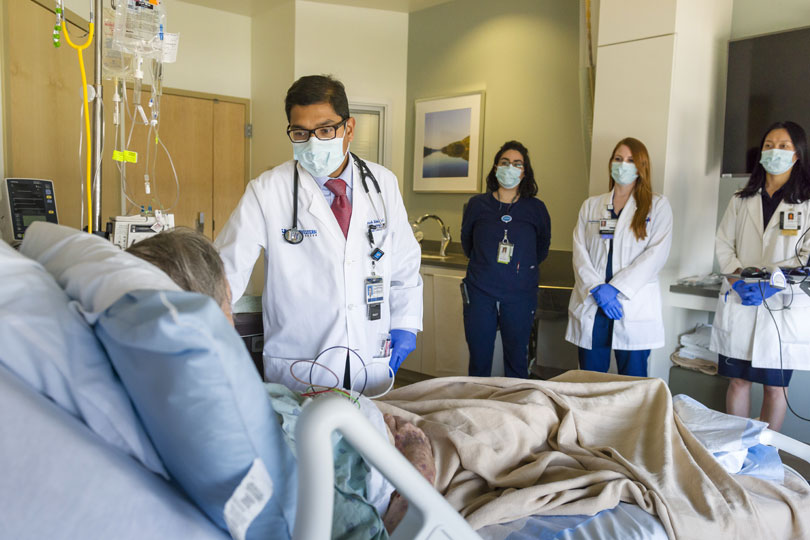 An attending physician and students wear masks as they attend to a patient in a hospital
