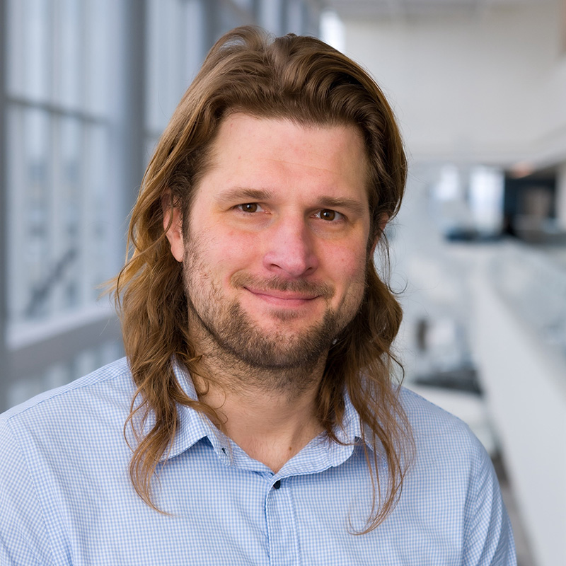 Smiling man with long brown hair, beard and mustache.