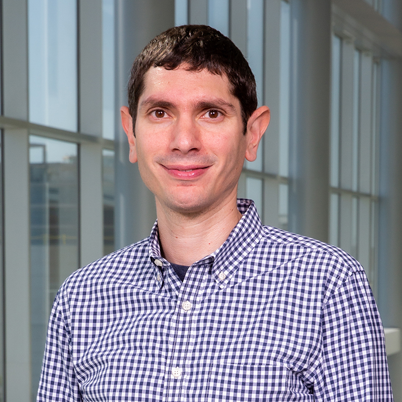 Smiling man with short, dark hair wearing a blue-checked shirt.