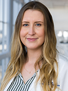 Woman with long, wavy blond hair wearing a white shirt with black stripes and white coat with UT Southwestern Medical Center logo