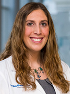 Woman with long, wavy brown hair wearing a grey shirt and white coat with UT Southwestern Medical Center logo