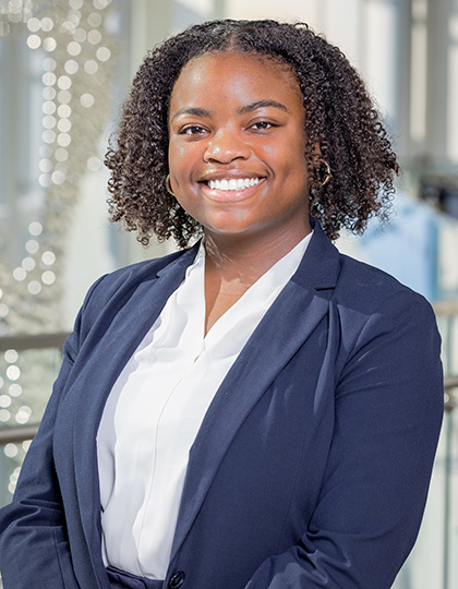 Smiling woman with dark, curly shoulder length hair, wearing a blue suit jacket over a white blouse.