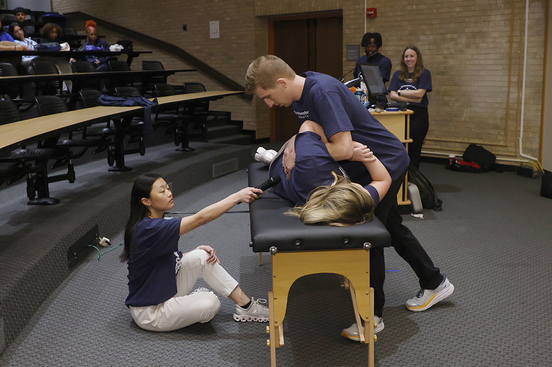 Male students performs chiropractic adjustment on female student who is lying on a massage table while other students observe