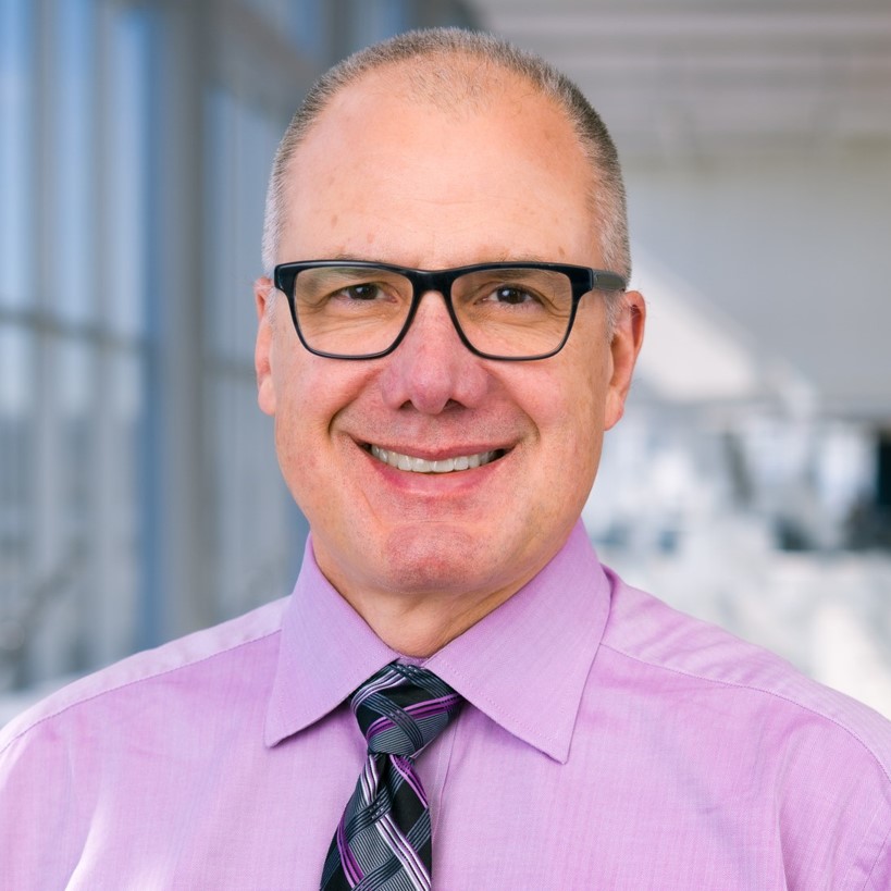 smiling man in a purple shirt and dark tie