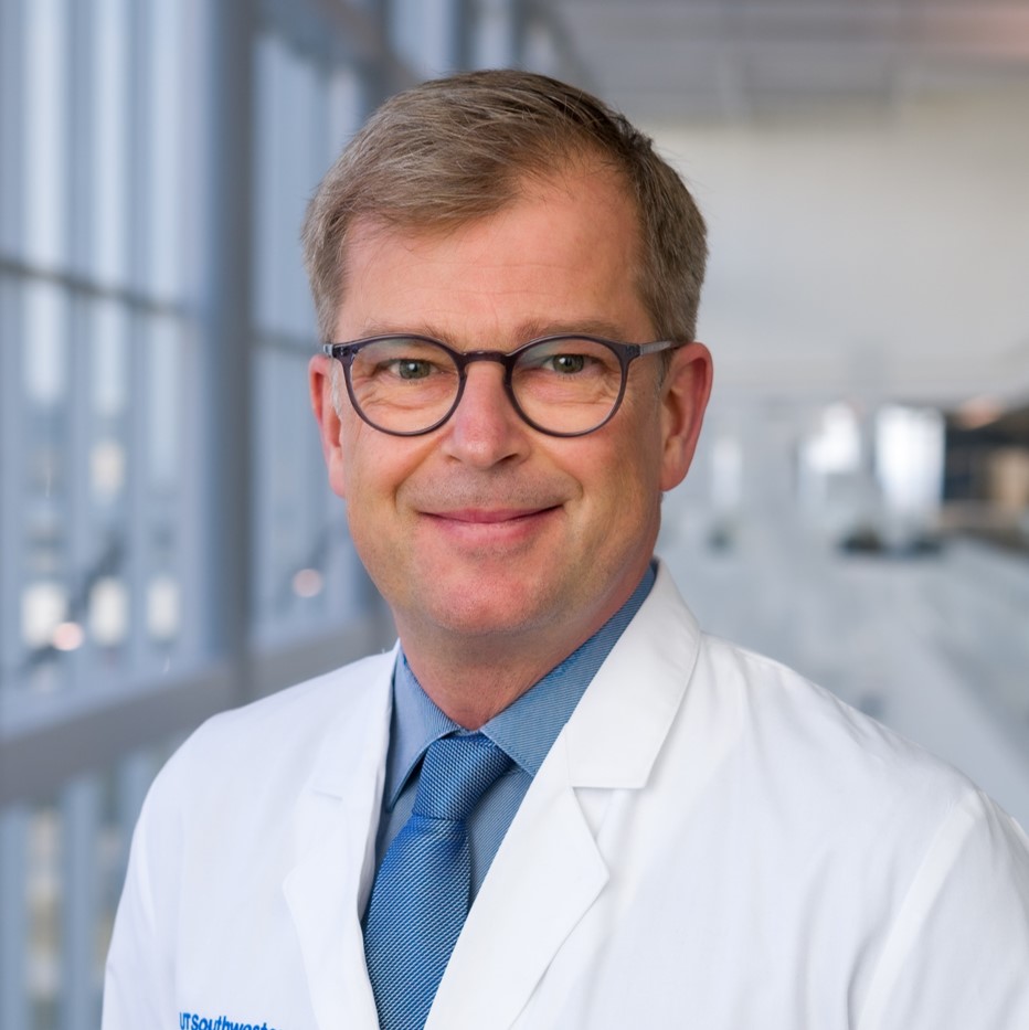 smiling man in a white lab coat with a blue shirt and tie