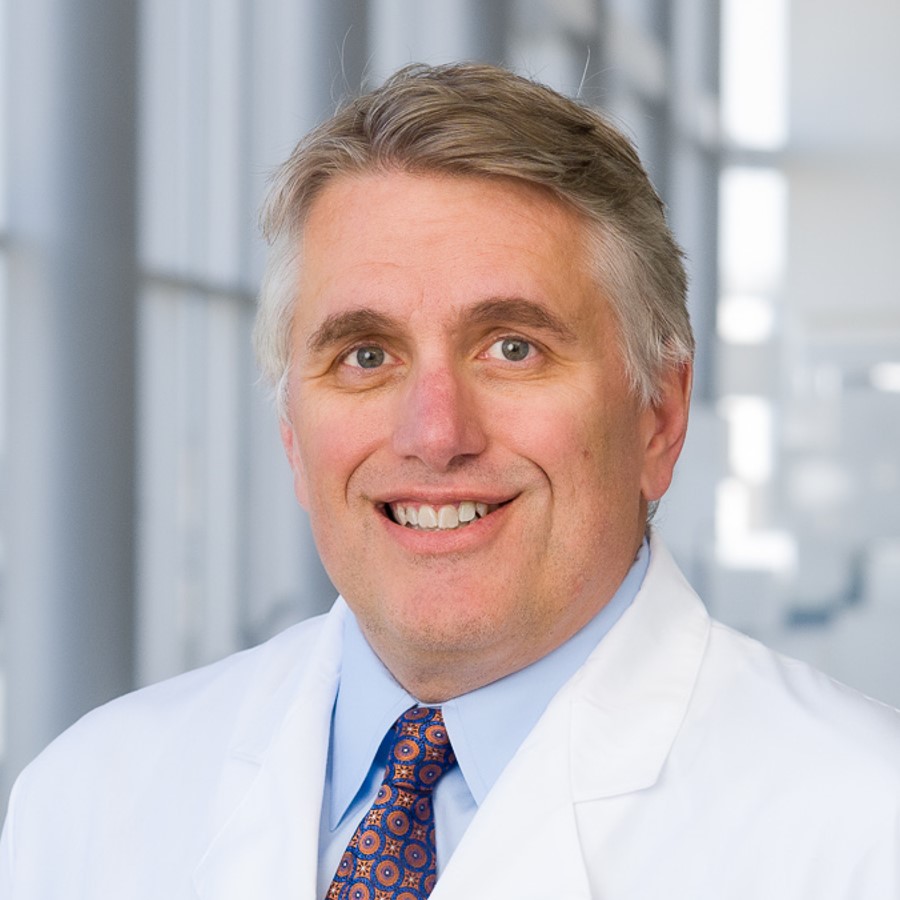 smiling man in a white coat with a light shirt and dark tie