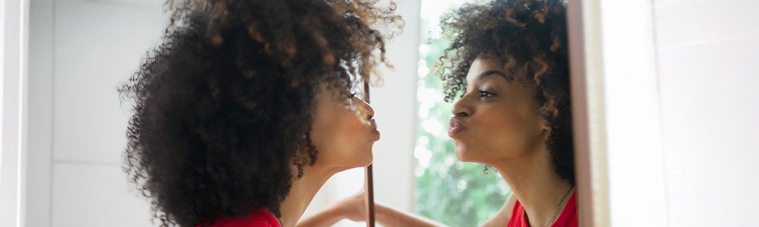 young black woman in red top kissing her reflection in a mirror