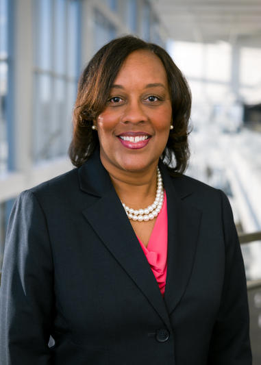 Smiling woman with straight hair wearing a black suit with pink shirt.