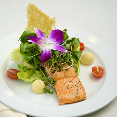 Plate with a meal of salmon topped with greens and a purple flower