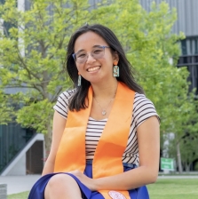 Smiling woman with long dark hair, wearing a sunglasses and a multi-colored striped shirt.