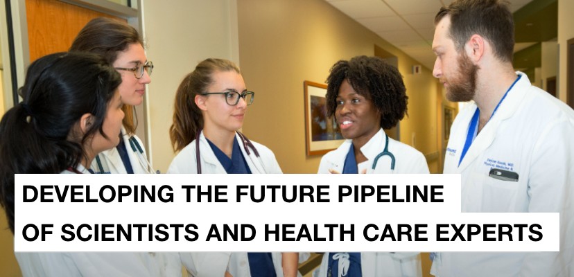 Five diverse men and women wearing white coats talk in a hallway and the message developing the future pipeline of scientists and health care experts