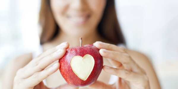 woman holding red apple with a heart carved in it