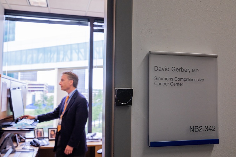 Dr. David Gerber stands by a computer in his office with his name on the door in the foregound