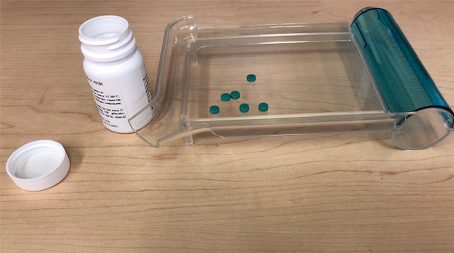 Pill counting tray with six round green tablets on it