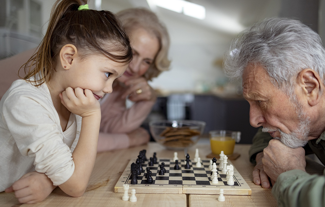 Young granddaughter plays chess with her grandpa as her grandmother looks on.