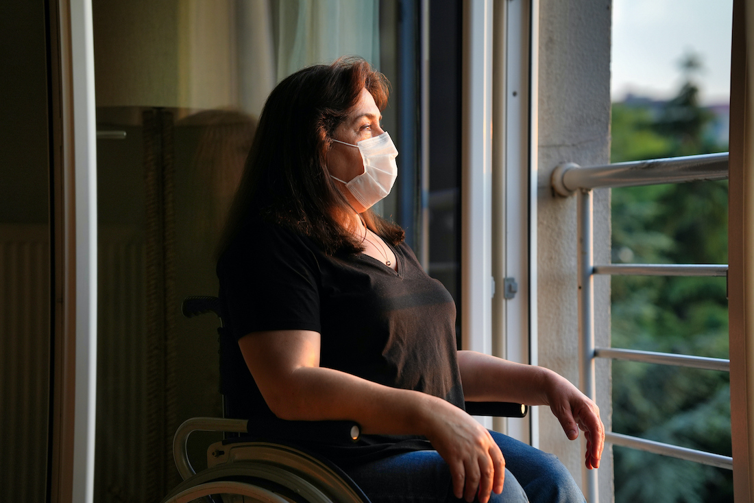 Disabled woman wearing a mask looking out of her window