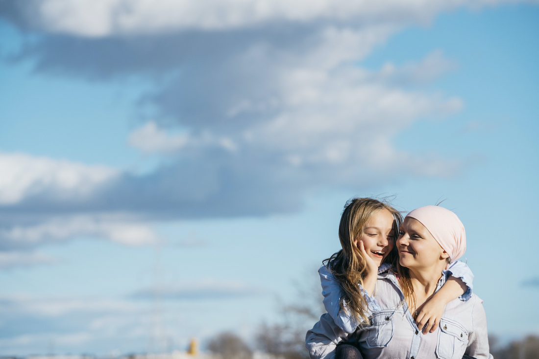 A woman with cancer is next to her daughter. A girl is hugging a woman happy