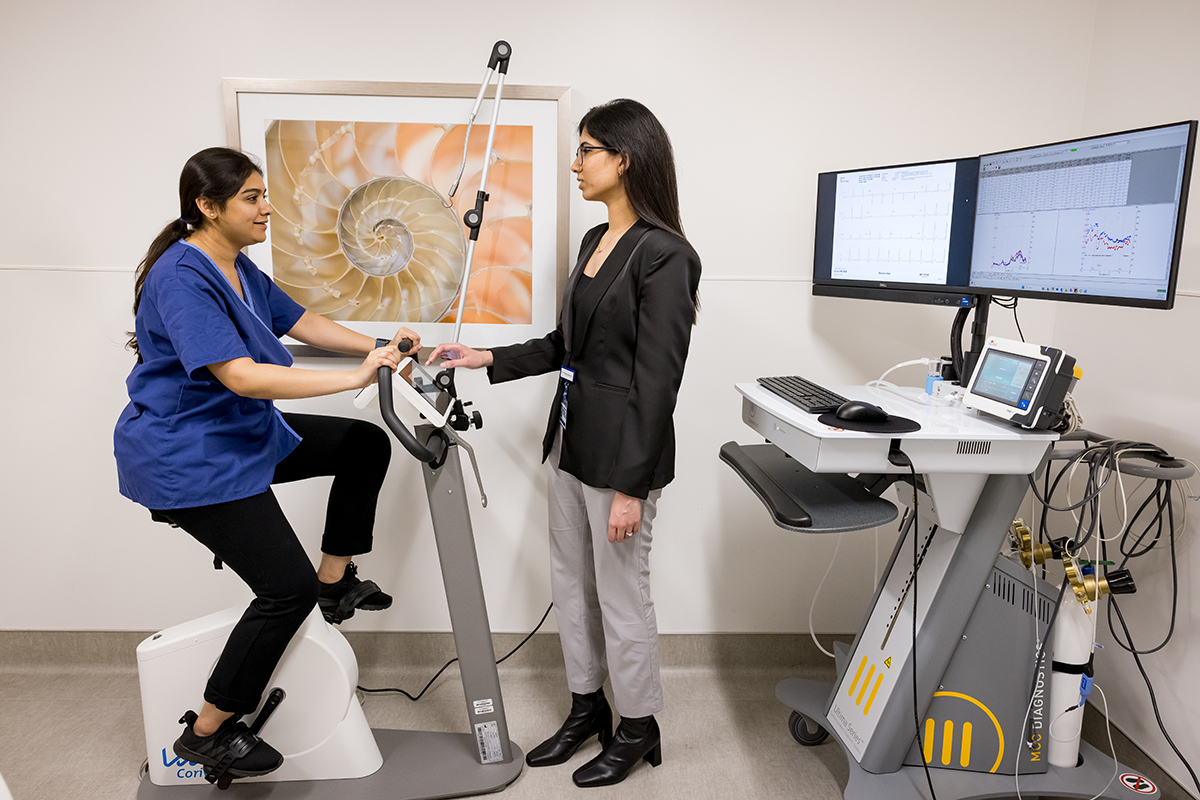 a woman riding a stationary bike hooked up to computer monitoring system with a woman observer