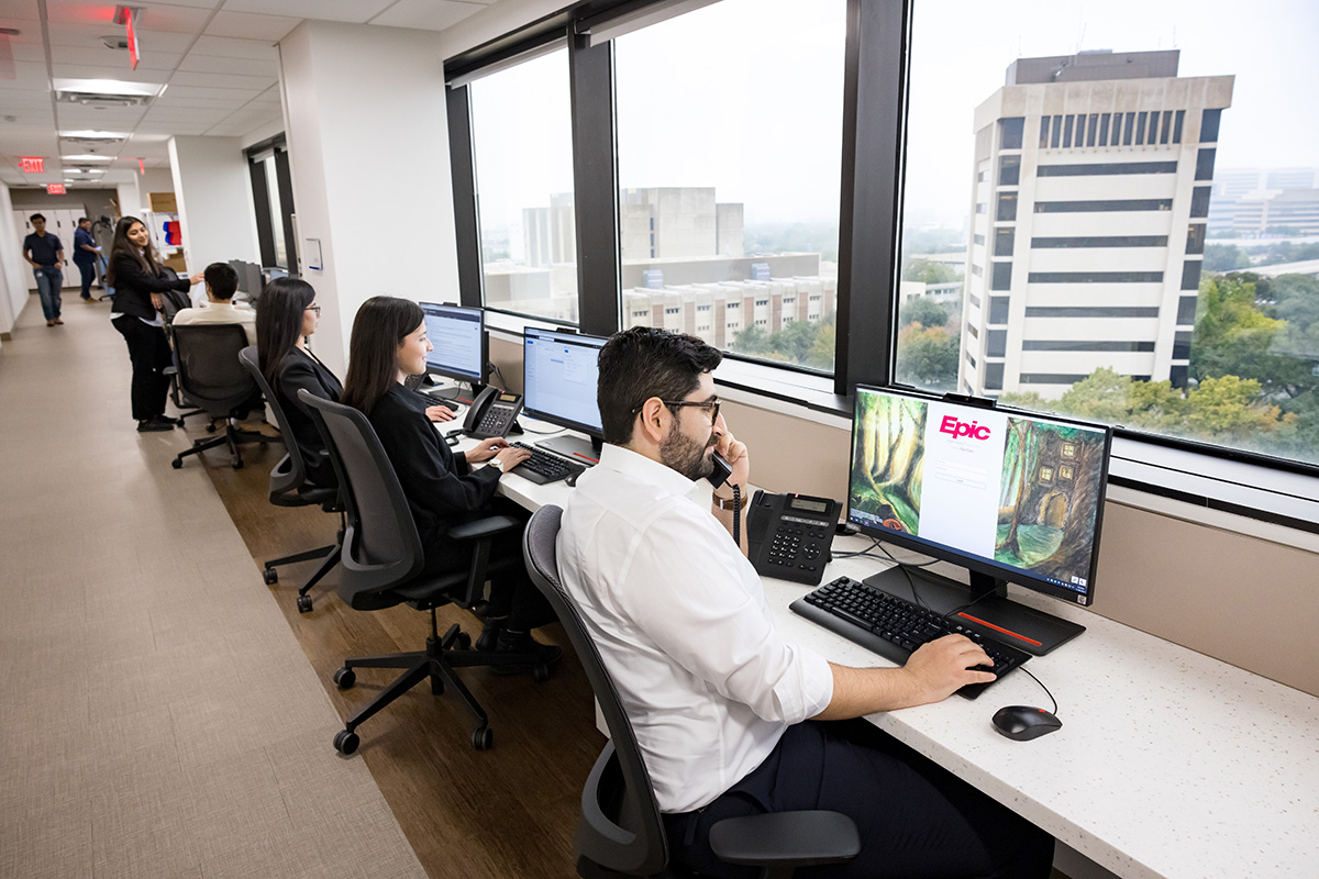 three people at computers infront of bank of windows