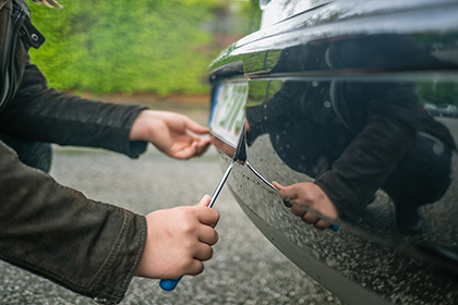 Close-up of a man's hands holding a screw driver and removing  license plate from the bumper of a car